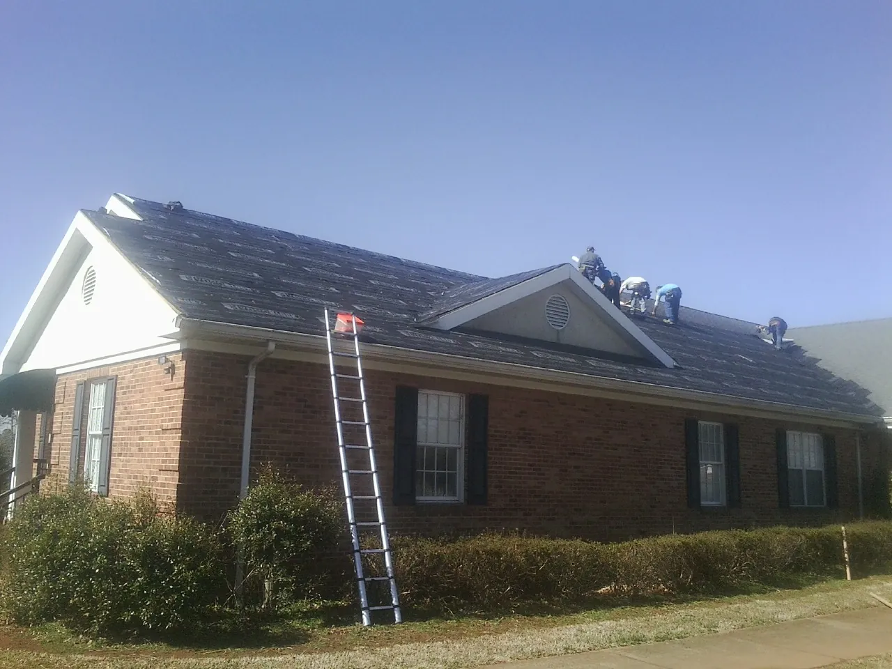 Crew tearing shingles off a brick ranch roof with a ladder set — Emergency Roof Repair work by our crew in Winneconne