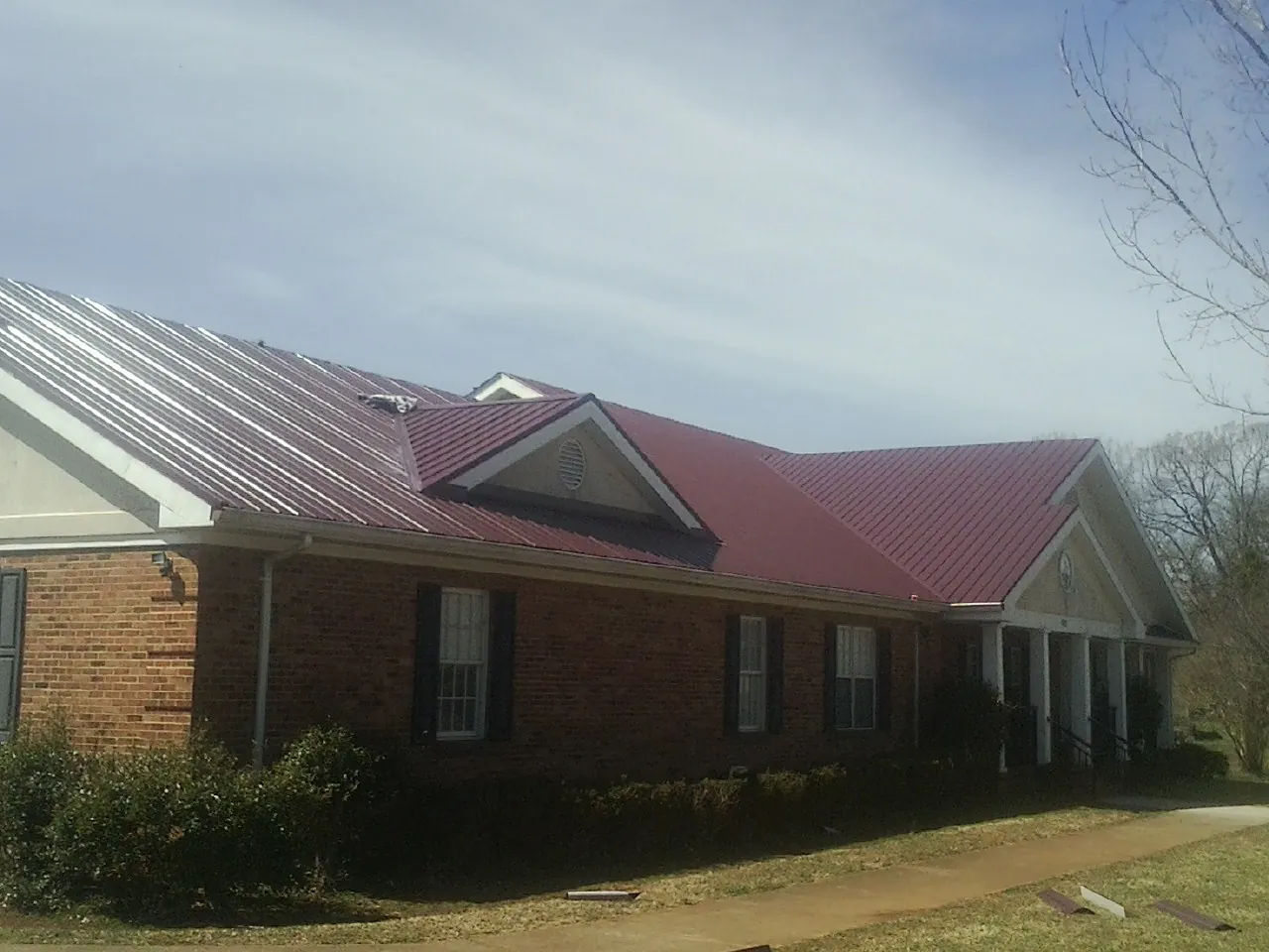 Red metal roof with gabled entries on a long brick building, from a Hail Damage Roof Repair job in Winneconne