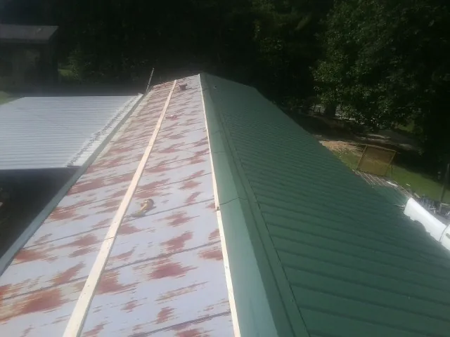 Old rusted panels beside newly installed green metal roofing — Wind Damage Roof Repair by Roofing Brothers in Winneconne