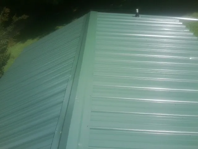 New green metal panels meeting at the ridge of a roof — Flat Roof Repair work by our crew in Winneconne