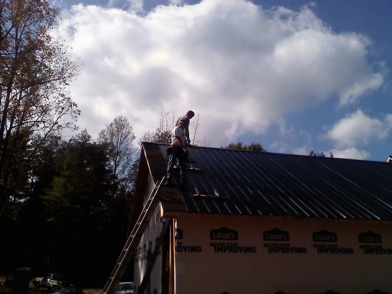 Roofer fastening dark metal panels high against a cloudy sky, from a Roof Inspection job in Winneconne