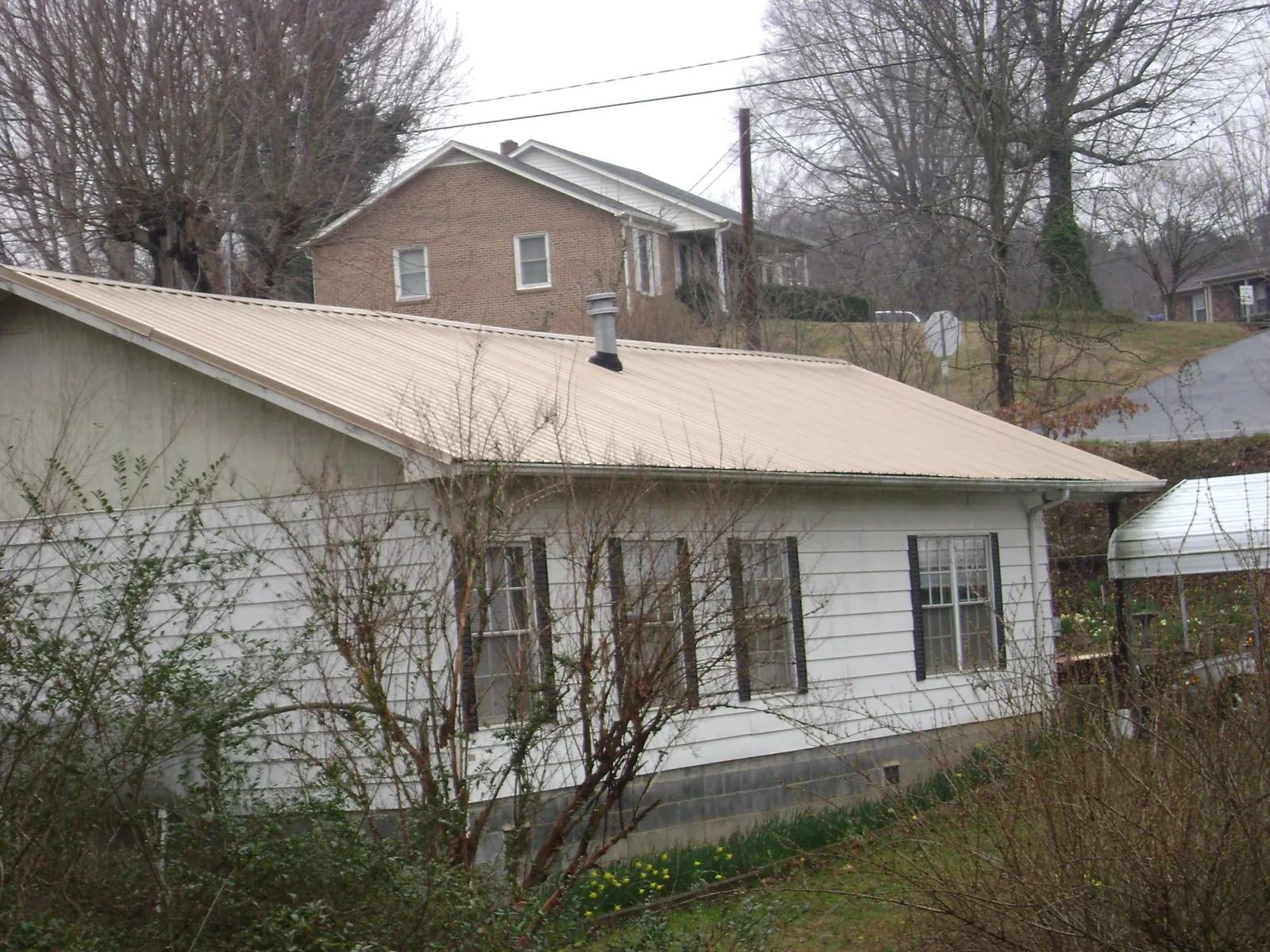 Tan metal roof on a white sided house set into a hillside — Commercial Roofing by Roofing Brothers in Winneconne