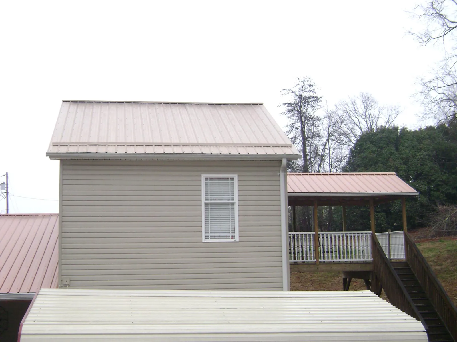 Tan metal roofs on a two story addition and attached porch, from a Roof Replacement job in Winneconne